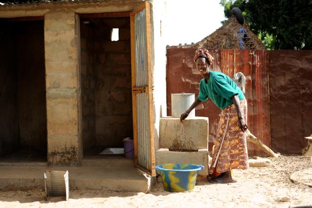 Femme devant un robinet d'eau et des latrines
