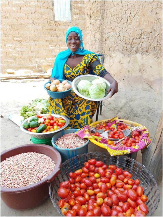 Femme prenant la pose derrière des bacs remplis de différents légumes