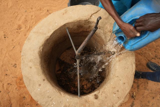 Personne vidant une jerricane d'eau dans un puits