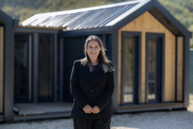 Business owner posing in front of the model house financed by the proejct