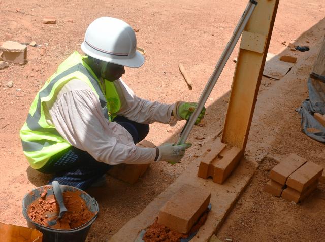 Femme à genou construisant un mur en briques rouges
